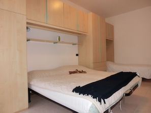 Une chambre avec un lit simple, une armoire en bois et une étagère au-dessus du lit.