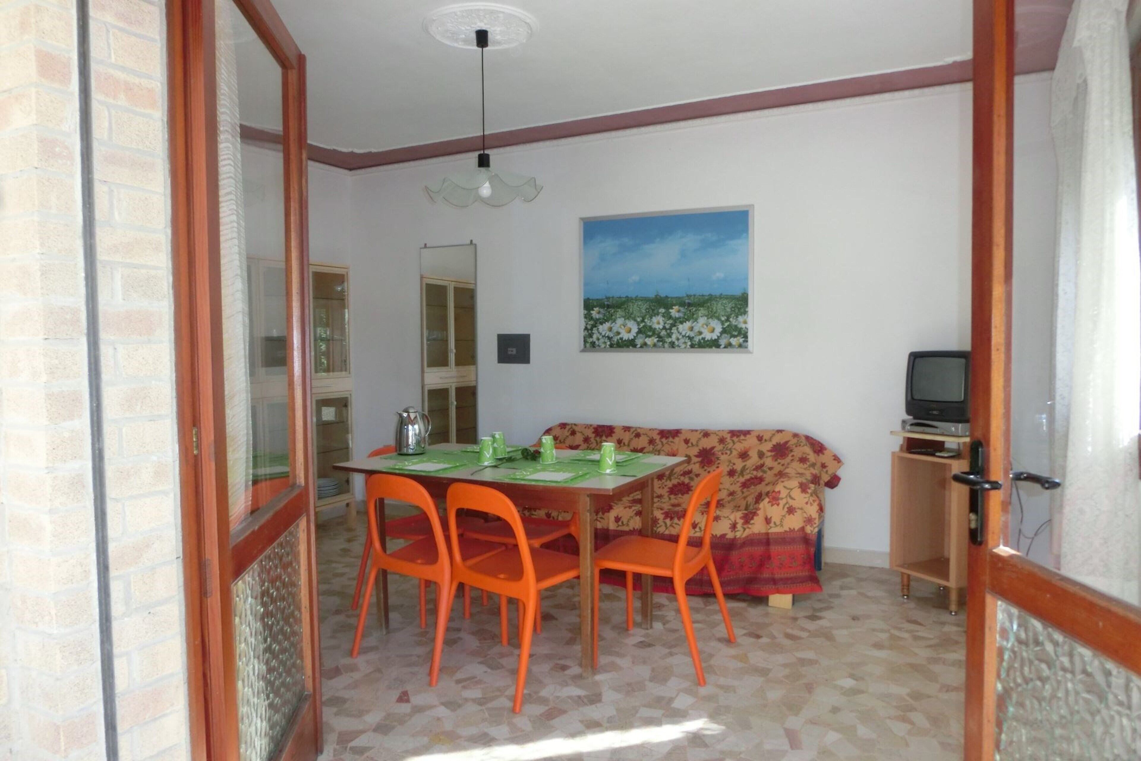 A dining area with a table and chairs, a sofa, a television, and a painting on the wall.