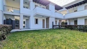 A modern multi-story residential building with a central courtyard, balconies, and a well-maintained lawn. - Wonderful Flat With Solarium and Swimming Pools (San Michele al Tagliamento)