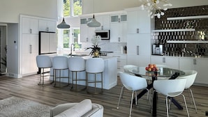 A modern kitchen with white cabinets, a central island with bar stools, and a dining area with a glass table and white chairs.