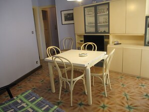 A dining area with a table and chairs, a kitchen with cabinets, and a patterned floor. - Grado Pineta Lovable Seaview Apartment (Grado)