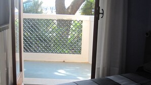 A room with a bed, a balcony with a lattice screen, and a view of greenery outside.