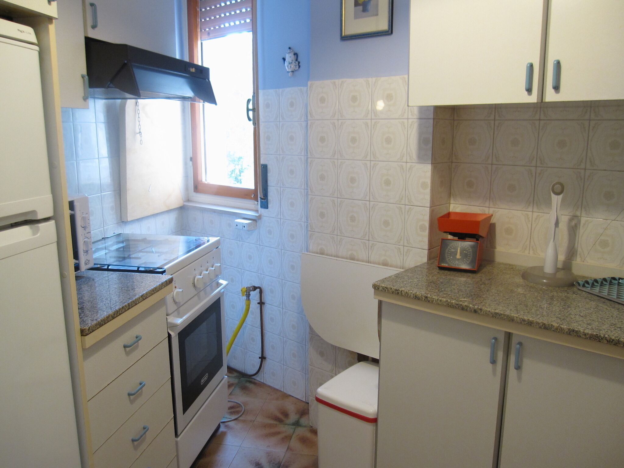 Cozinha compacta com armários brancos, fogão, forno, janela e pia.