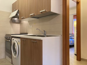 Een kleine keuken met houten kastjes, een ingebouwde wasmachine en een roestvrijstalen spoelbak.