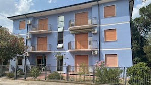 Un immeuble résidentiel à plusieurs étages, doté de balcons, de climatiseurs et d’une entrée sécurisée par un portail.