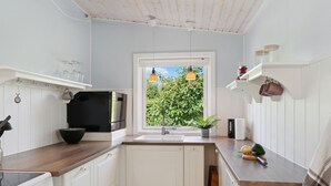 Et køkken med hvide skabe, et sort køleskab, en komfur og et vindue med udsigt til grøn vegetation.