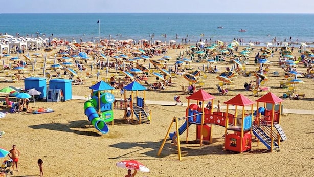 A crowded beach with numerous umbrellas, a children's play area, and a clear view of the sea. - Cosy One Bedroom Flat Near the Beach - Reserved Parking Space by Beahost (San Michele al Tagliamento)