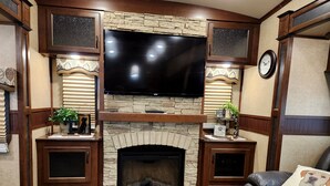 A living room with a stone fireplace, a flat-screen TV, wooden cabinets, and a leather couch.