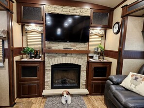 A living room with a stone fireplace, a flat-screen TV, wooden cabinets, and a leather couch.