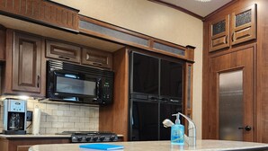 A kitchen with wooden cabinets, a black refrigerator, a microwave, and a sink.