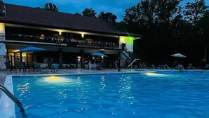 A swimming pool with a covered deck area, lounge chairs, and umbrellas.