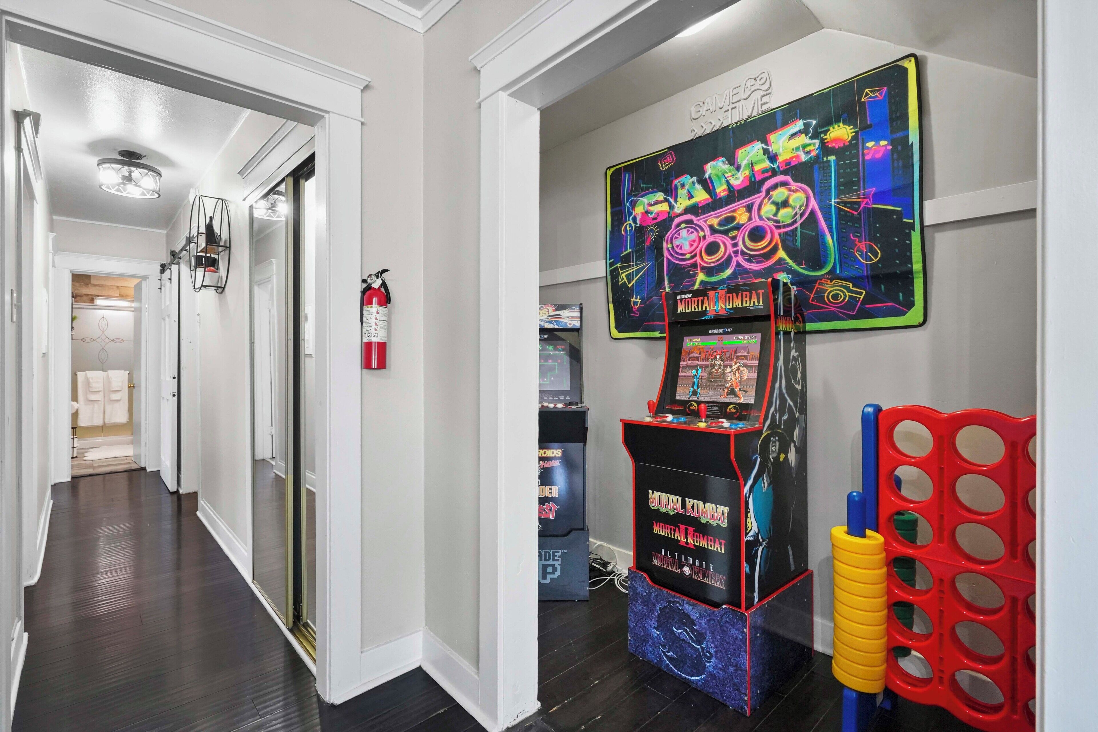 A hallway with a neon arcade game, a fire extinguisher, and a water cooler.