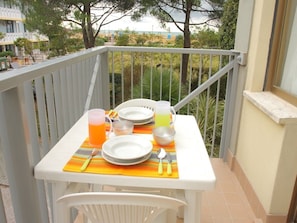 Un balcon avec une table dressée pour deux personnes, comprenant assiettes, couverts et boissons.