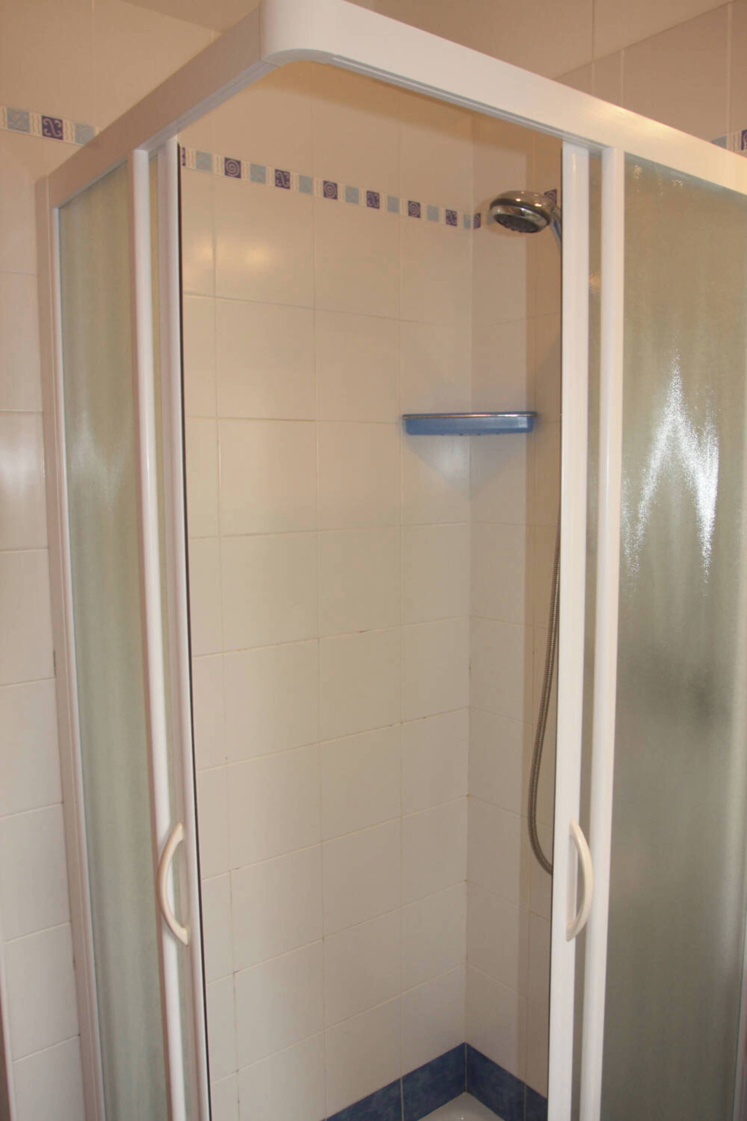Eine bodenebene Dusche mit satinierten Glastüren, weißen Fliesenwänden und einem blau gefliesten Boden.