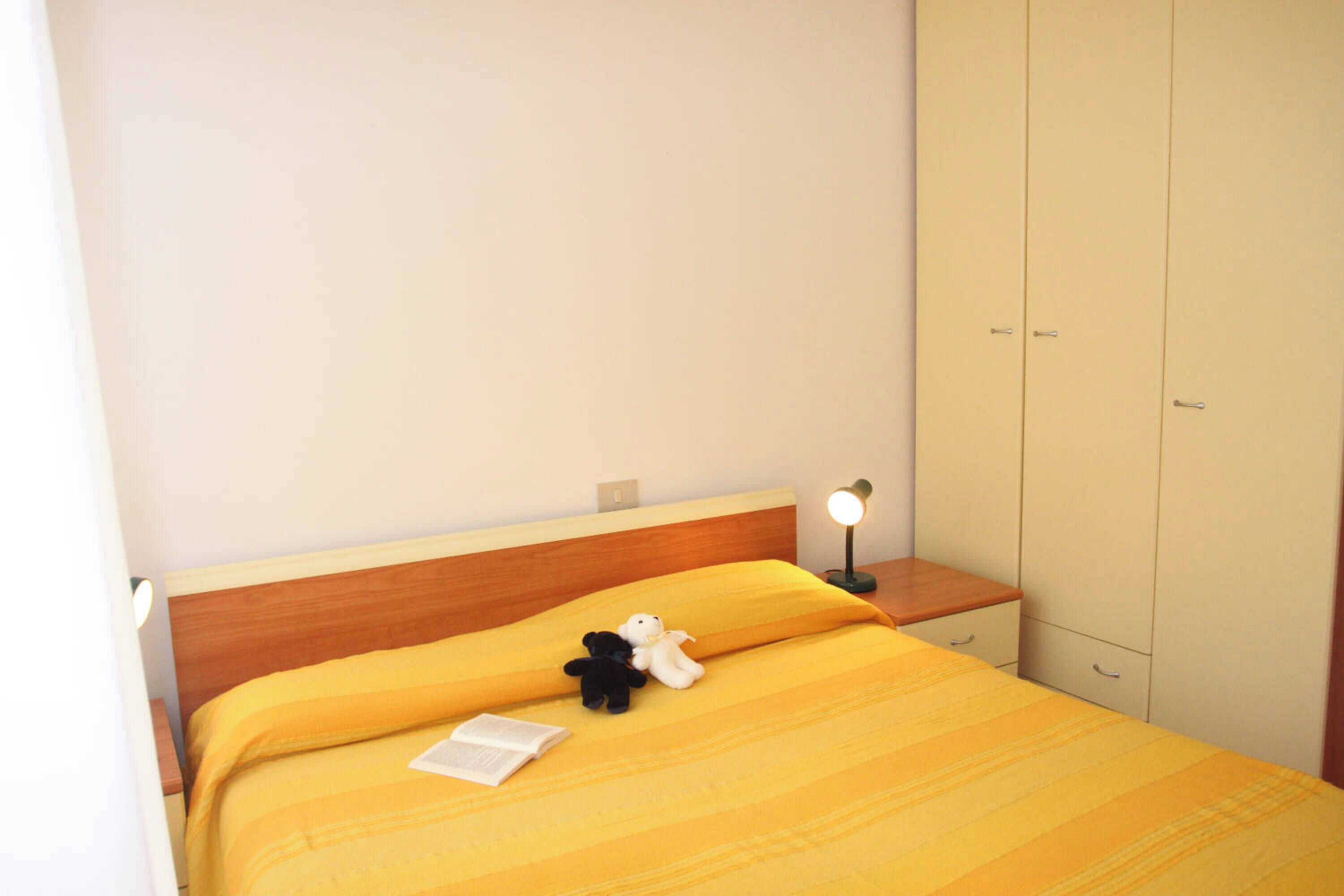 Ein Bett mit gelber Bettdecke, eine Nachttischlampe, ein Nachttisch und ein Kleiderschrank.