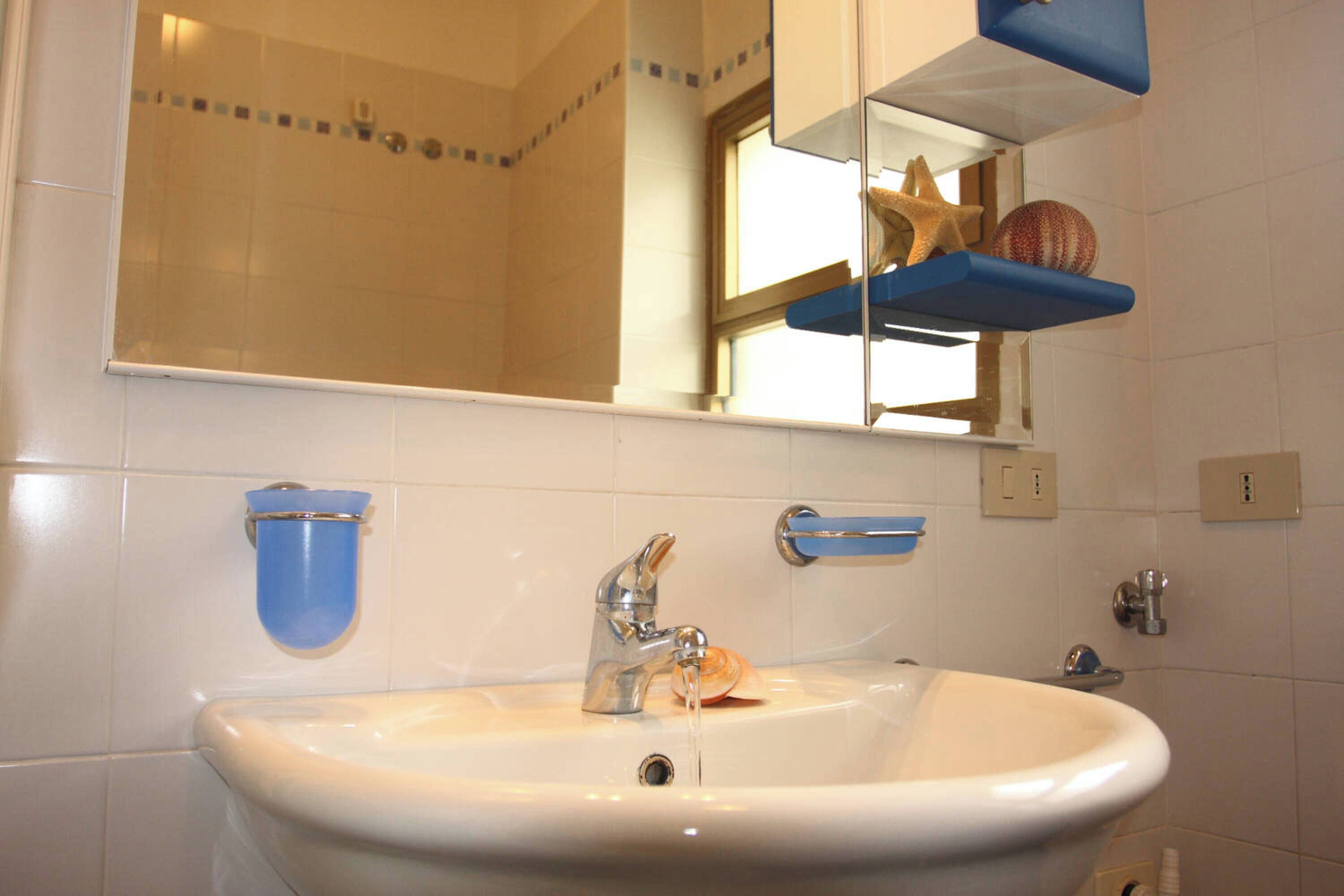 A bathroom with a white sink, a mirror, and a blue shelf with decorative items.