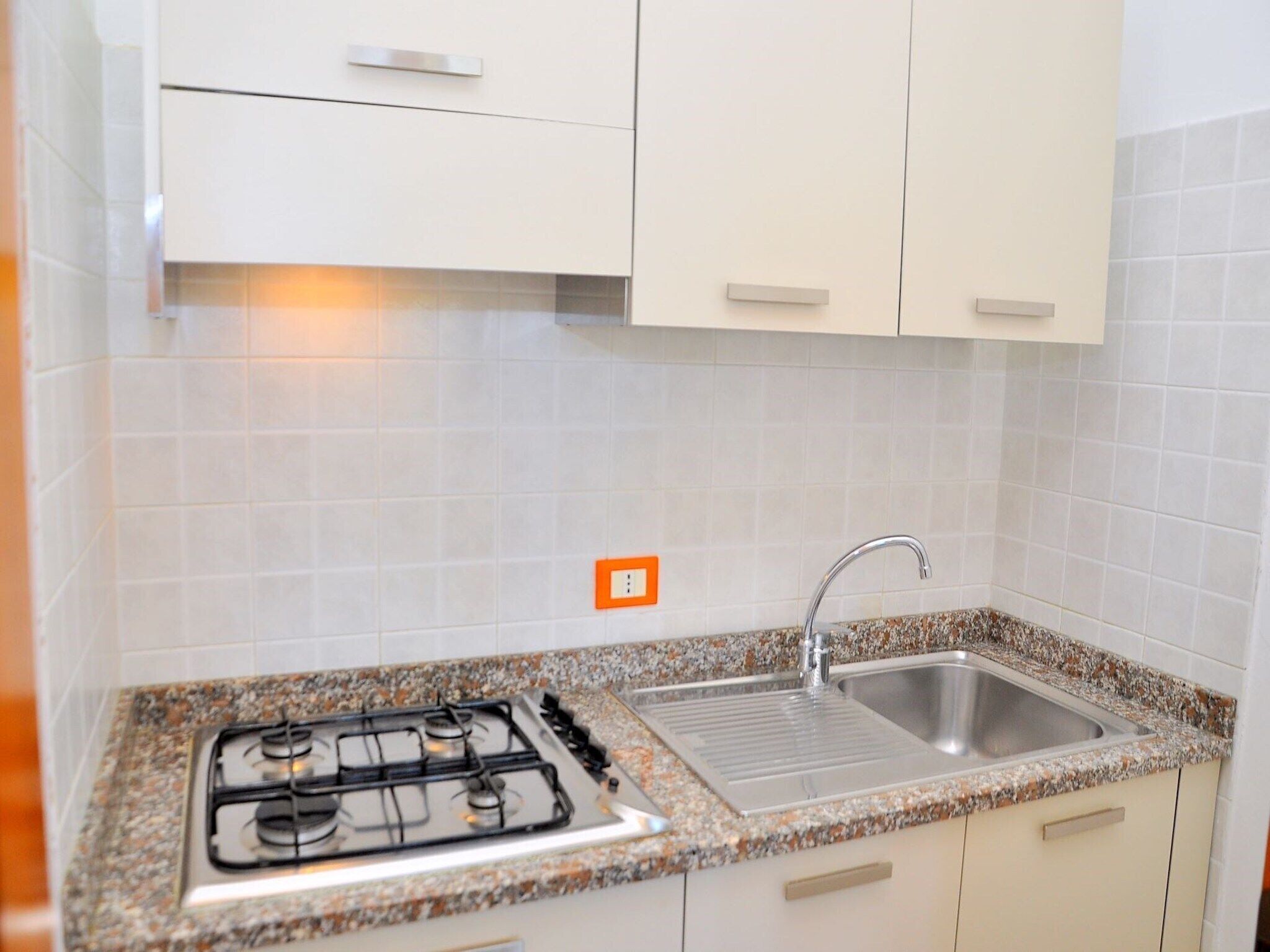 Una cocina con armarios blancos, encimera de granito, pileta de acero inoxidable y cocina a gas.