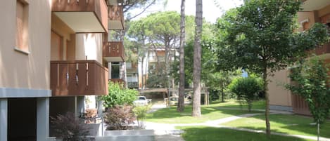 A courtyard with a pathway, trees, and a building with balconies.
