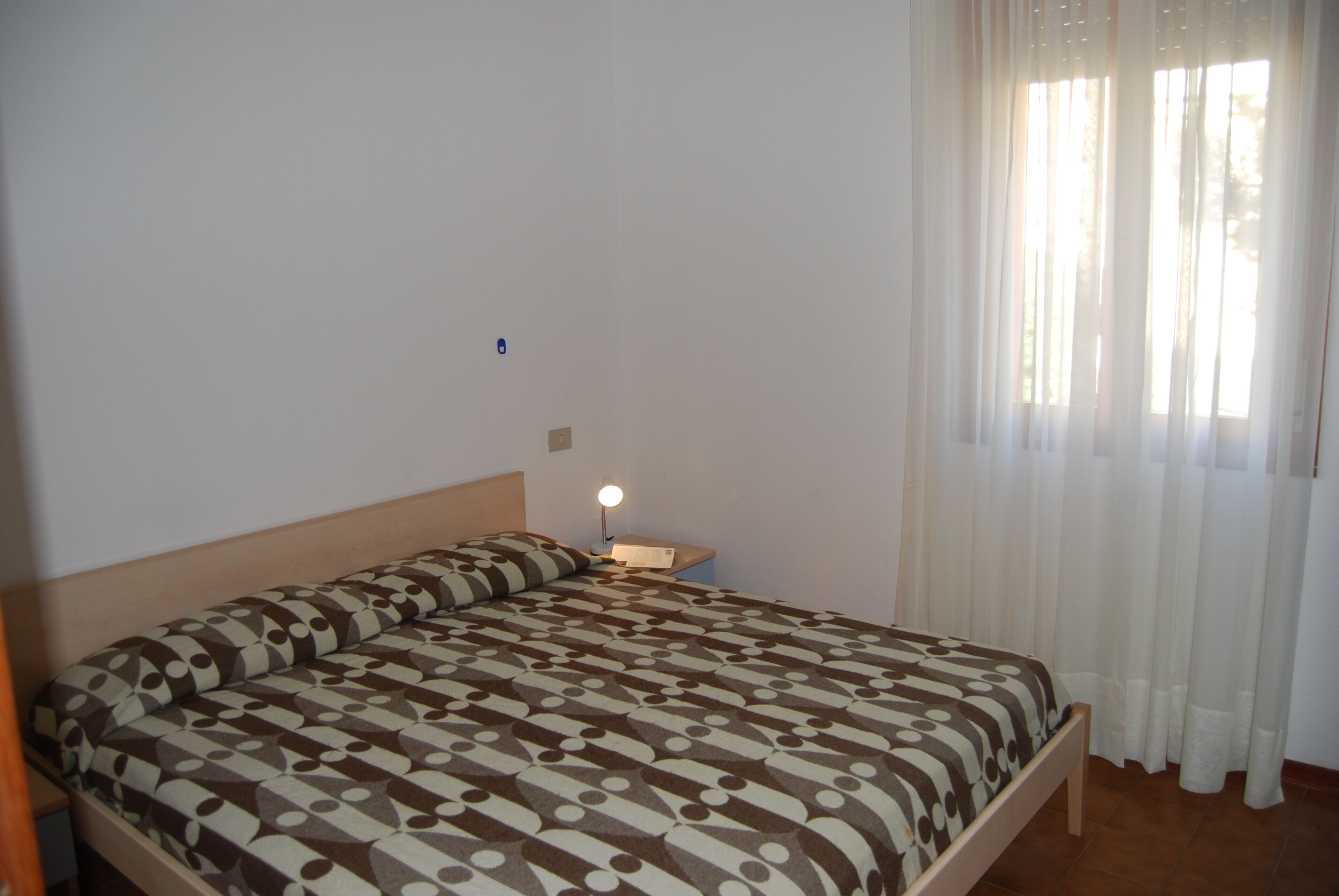 Un dormitorio con una cama, una mesita de noche con lámpara y una ventana con cortinas.