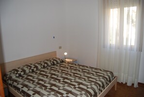 Ein Schlafzimmer mit einem Bett, einem Nachttisch mit Lampe und einem Fenster mit Vorhängen.