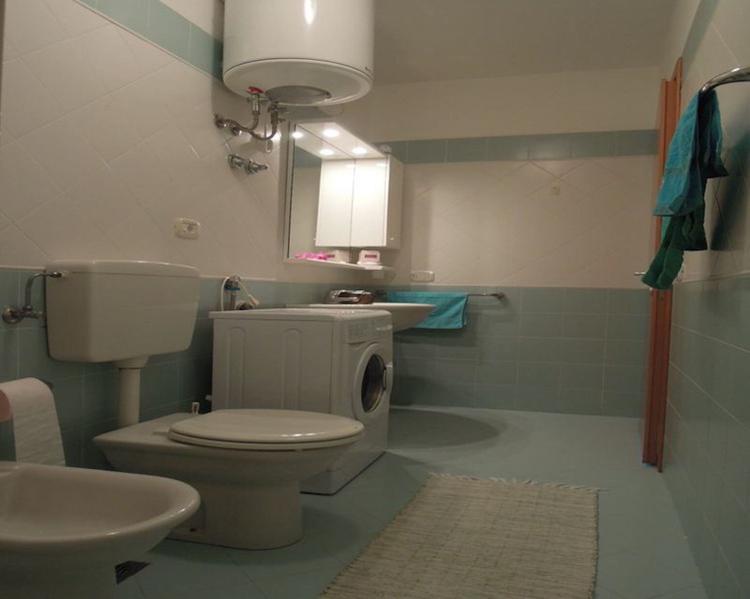 A bathroom with a toilet, washing machine, sink, and a mirror.