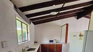 A compact kitchen with a stove, microwave, and refrigerator, wooden beams on the ceiling, and a window with blinds. - Amisfield motel (Tokoroa)