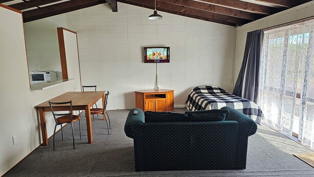 A room with a wooden ceiling, a bed with a checkered blanket, a sofa, a desk with a chair, and a television on the wall. - Amisfield motel (Tokoroa)