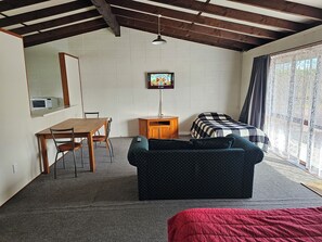 A room with a wooden ceiling, a bed with a checkered blanket, a sofa, a desk with a chair, and a television on the wall. - Amisfield motel (Tokoroa)