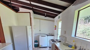 A compact kitchen with a refrigerator, washing machine, and stove. There is a window providing natural light and a view of the outdoors. - Amisfield motel (Tokoroa)