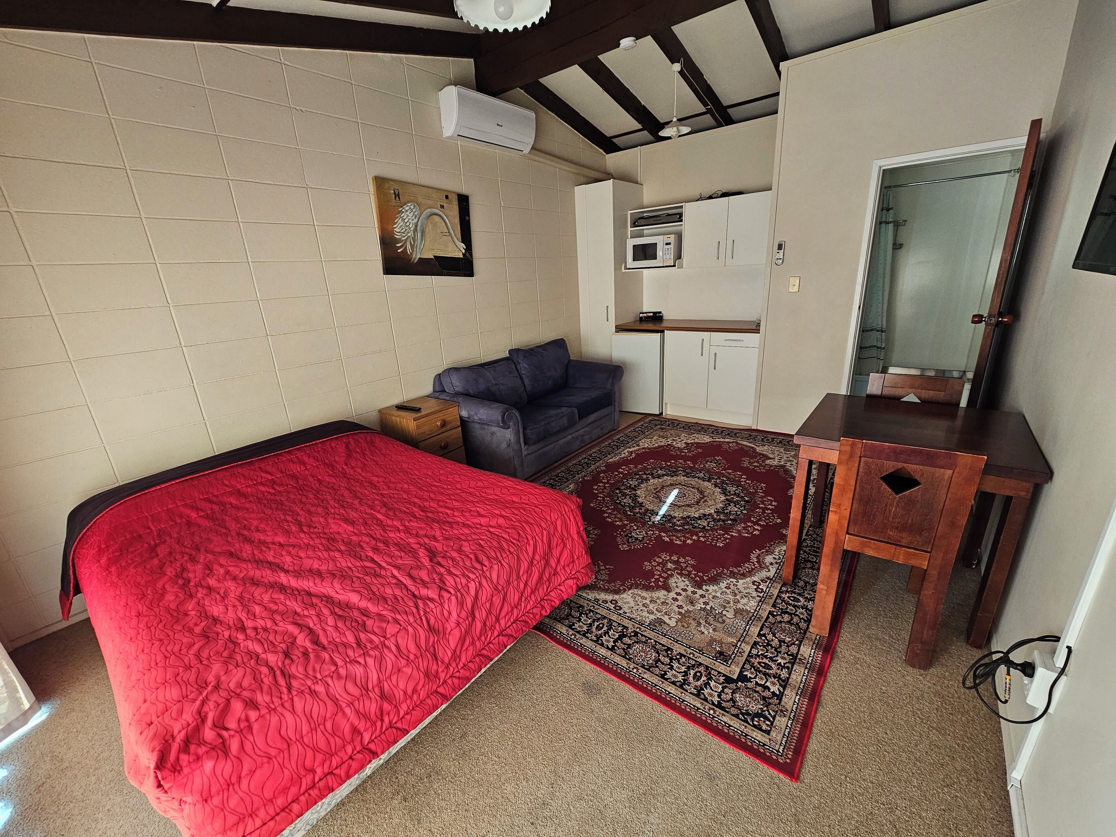 A compact room with a bed, a sofa, a small table, a microwave, and a cabinet.