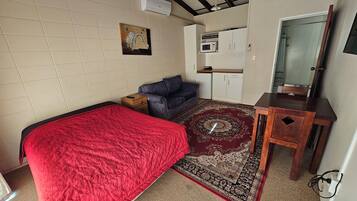 A compact room with a bed, a sofa, a small table, a microwave, and a cabinet.