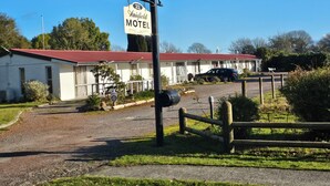 A motel with a red roof, a signboard, and a parked car. - Amisfield motel (Tokoroa)