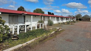 A row of white mobile homes with red roofs, each featuring a porch and a small garden area. - Amisfield motel (Tokoroa)