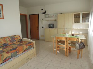 Un salon avec un canapé, une table à manger avec des chaises, un coin cuisine avec des placards, un téléviseur et une porte.