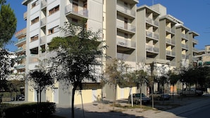 Un edificio residenziale a più piani con balconi, un'area di parcheggio e alberi sullo sfondo.