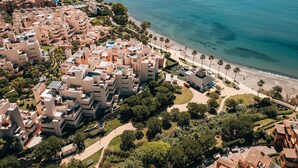 Vue aérienne d’un quartier résidentiel situé sur la côte, avec des bâtiments modernes, une plage et des palmiers.