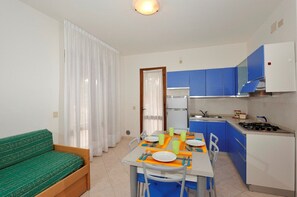 A compact kitchen with blue cabinets, a dining table set for two, and a green sofa.