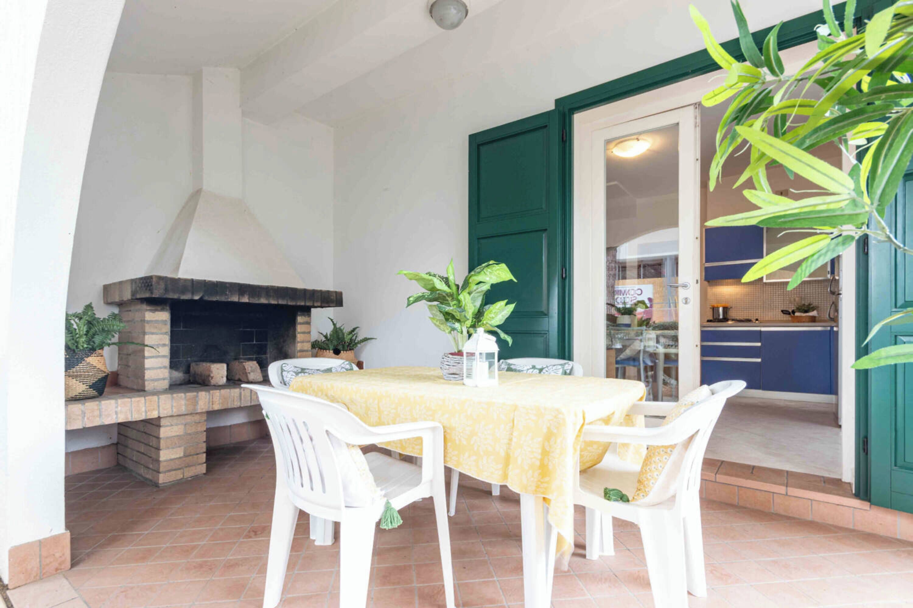 Un patio con chimenea de ladrillo, una mesa de comedor con sillas y una cocina visible a través de una puerta de vidrio.