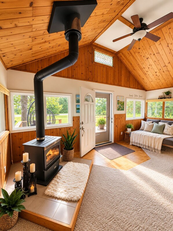 Une pièce chaleureuse avec un poêle à bois, un ventilateur de plafond et un lit donnant sur le paysage extérieur.