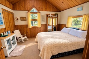 Un dormitorio acogedor con una cama grande, paredes de madera, un sillón mecedora y una ventana con cortinas.