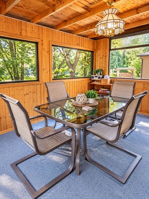 Una habitación con paneles de madera, una mesa con superficie de vidrio, cuatro sillas, una radio y una estantería.