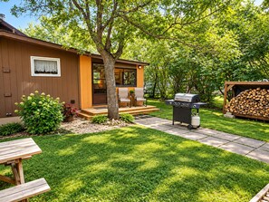 Patio trasero con una parrilla, una terraza de madera y una casa con una ventana.