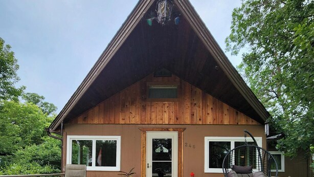 Eine Holzhütte mit Satteldach, einer Haustür und einer Veranda mit zwei Stühlen und einer Schaukel.