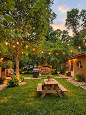 A backyard with a wooden deck, a barbecue grill, string lights, and a picnic table.