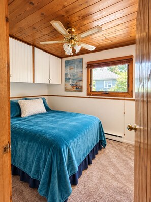 A bedroom with a bed, a ceiling fan, a window, and a painting on the wall.