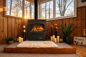 Una habitación acogedora con estufa de leña, una alfombra mullida, velas y una planta en maceta.