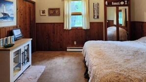 Ein Schlafzimmer mit Holzwandverkleidung, Deckenventilator, Bett, Schminktisch, Fenster mit Vorhängen und einem Spiegel mit dem Schild 'Beach'.