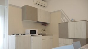 A compact kitchen with a microwave, a refrigerator, and a sink. There is a dining table with chairs and a decorative item on the wall. - One-bedroom Flat With Balcony and AC (San Michele al Tagliamento)
