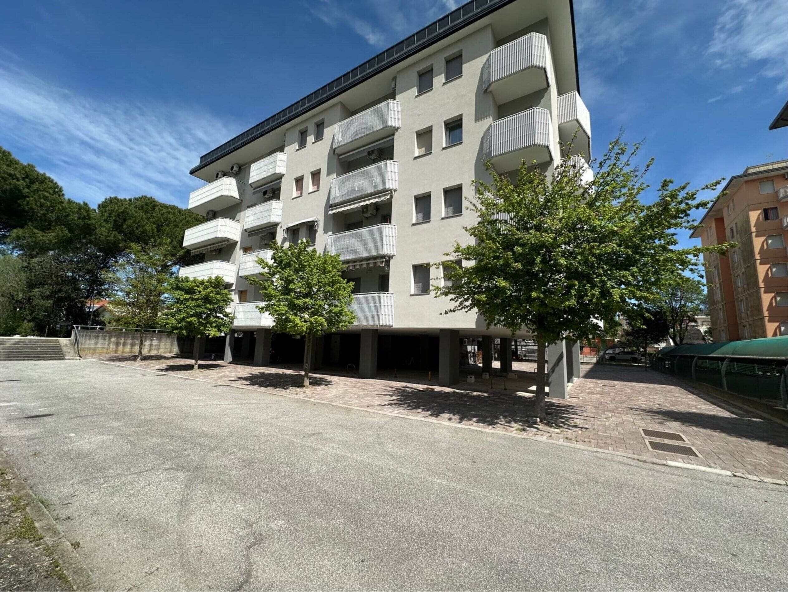 Ein mehrstöckiges Gebäude mit Balkonen, einem gepflasterten Parkplatz und Bäumen.