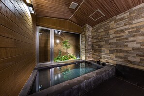 A modern bathroom with a glass-enclosed hot tub, wooden panel walls, and a stone-tiled shower area. - Almeria Hotel (Yamanakako)
